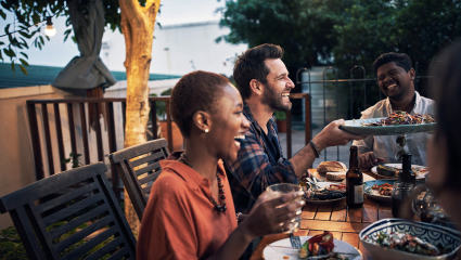 A group of friends make a happier home as they laugh and eat a meal in their backyard.