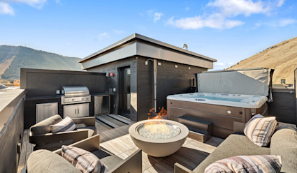 A rooftop deck with a fire pit, lounge seating, hot tub and BBQ.