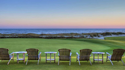 A serene Kiawah Island beach scene at sunset with Adirondack chairs on a manicured lawn, sand dunes, and soft pastel sky colors. This image highlights the island's relaxing coastal ambiance and sets an inviting tone for an ultimate events and activities guide.