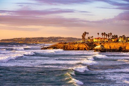 Crashing ocean waves in front of a large luxury home at dusk