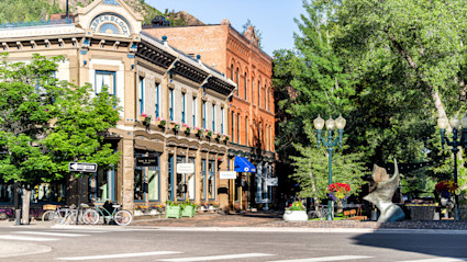 A vibrant summer street scene in Aspen, Colorado, with historic brick buildings, flower boxes, and bicycles, capturing the lively and charming small-town mountain atmosphere.