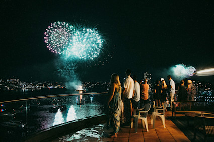 A group of people watching fireworks from a large balcony.