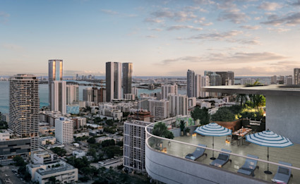 Expansive penthouse terrace with lounge chairs and striped umbrellas overlooking Miami's skyline, bay, and ocean at dusk.