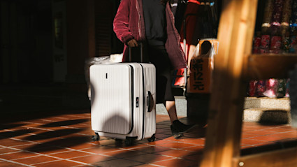 Woman walking with a white roller suite case over a red brick floor.