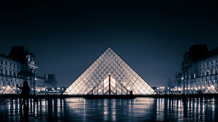 The illuminated glass pyramid of the Louvre Museum in Paris at night, surrounded by the grandeur of historic architecture and city life, encapsulates the essence of Paris as a global cultural capital known for its art, history, and vibrant ambiance.