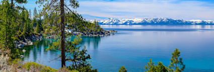 View of Lake Tahoe during the spring with green pine trees and snow covered mountains in the distance.