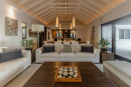 Open-concept living area with white sofas, vaulted wood ceilings, and a view into the kitchen at a St. Barth home.
