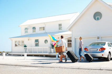 Travelers carry their luggage into their beachside rental unit, confident they received the best deal after comparing Vrbo vs Airbnb.