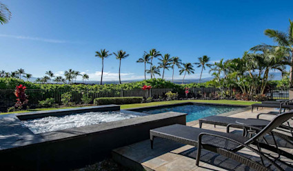 Outdoor lounge area with hot tub and plunge pool and poolside lounge chairs with surrounding hedges and palm trees.