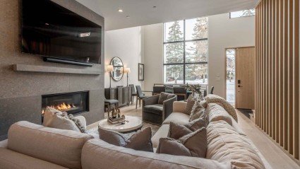 A spacious second home living room with a neutral color scheme, featuring a sectional sofa, accent chairs and a wall-mounted TV.