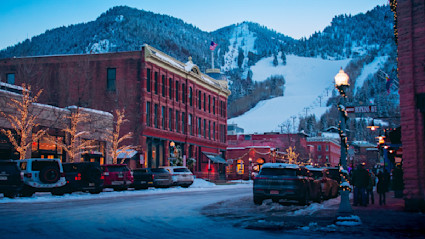 Snow-dusted street in Aspen with festive lights and nearby ski terrain, capturing the spirit of an alpine holiday.