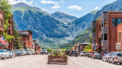 A vibrant street scene in Telluride, Colorado, with the backdrop of stunning mountains, festive flags, and historic buildings, perfectly capturing the lively and picturesque atmosphere that comes alive during the Telluride Film Festival.