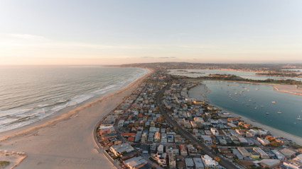 Aerial view of San Diego's coastline at sunset, featuring beachfront homes and sailboats, reflecting the luxury and vibrant lifestyle central to the city's food and wine festival.