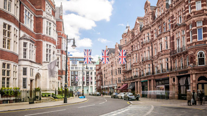 A street view of a block in Mayfair, London, featuring cars and British flags.