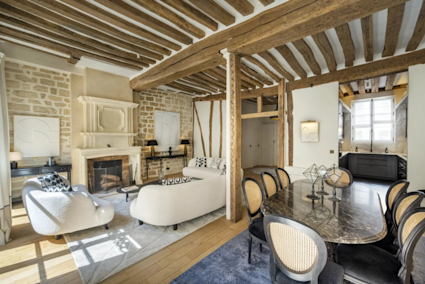 The dining area at Rue du Bac in Paris combines beamed ceilings, a stone fireplace, and a semi-open kitchen, creating a sophisticated setting for memorable meals and gatherings in the heart of the city.