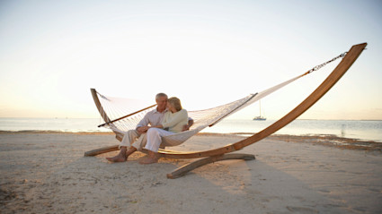 A couple relaxing in a hammock against the backdrop of the ocean reflects the essence of a private summer escape, evocative of the exclusivity and calm found in luxury beachfront homes.