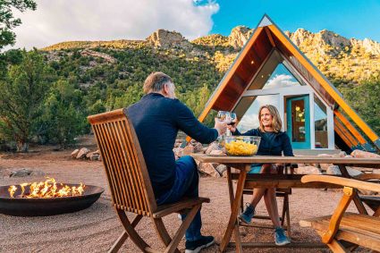 A married couple drinks wine next to a campfire at the A-frame rental they found from one of the best Airbnb alternatives. 