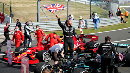 F1 driver, Lewis Hamilton, standing on his F1 car waving a British flag.