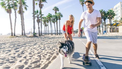 A couple skateboards with their dog near the ocean at Huntington Beach, a fun activity for pet-friendly vacations.