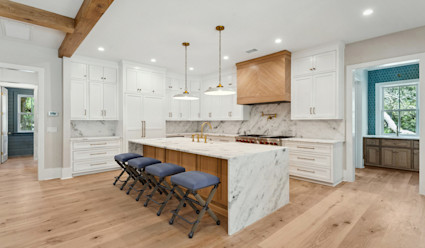 A kitchen with a marble island and backsplash with white cabinets and wood floors.