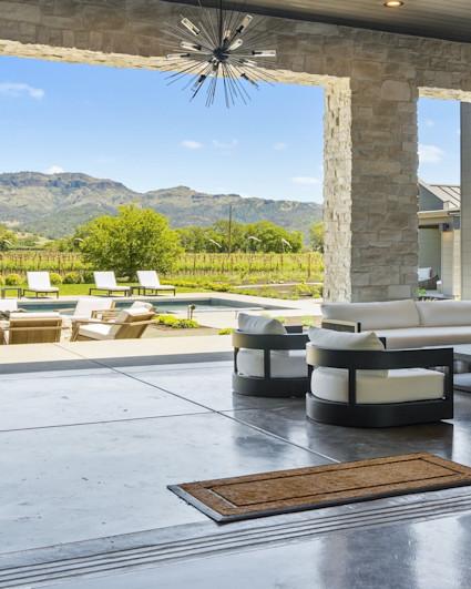 Living area of Napa luxury home looking out from the living area into the covered outdoor area with stonework and pool area with mountain in the background. 