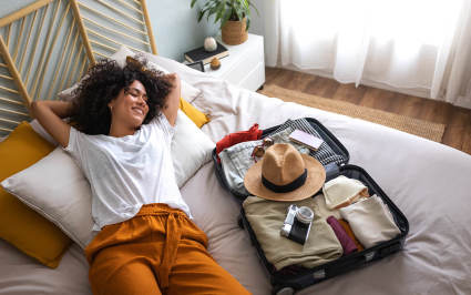 A person rests comfortably on a bed near an open suitcase.