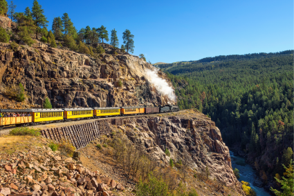 A yellow train traveling around a cliffside