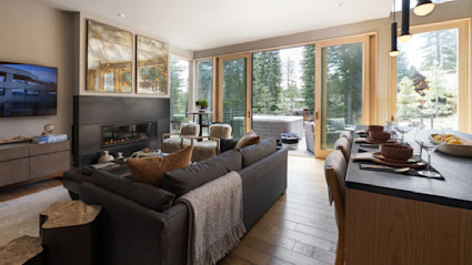A living room with floor to ceiling windows showcasing a porch with a hot tub and a forest view.