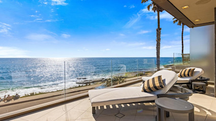 Beachfront patio in La Jolla with striped lounge chairs and ocean views, reflecting the tranquil, high-end lifestyle that pairs effortlessly with the La Jolla Concours d'Elegance.