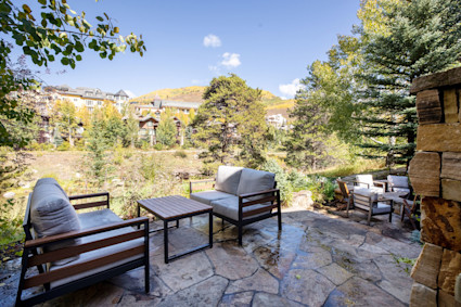 An outdoor lounge area on a patio with a fire pit and mountain views at a luxury home in Vail, ideal for apres-ski gatherings.