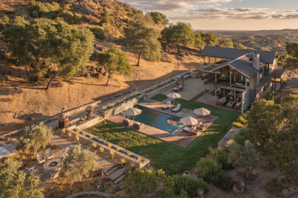 Aerial view of a hillside Napa home with a pool, lawn, and fire pit overlooking the valley at sunset.