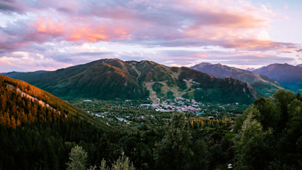 A breathtaking mountain sunset over Aspen, Colorado, with lush spring greenery and the town nestled in the valley below. This visually stunning scene captures the allure and natural beauty of a luxury mountain destination, making it ideal for travelers planning a spring ski getaway.