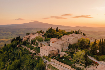 Tuscan hilltop village bathed in golden sunset light, stone villas nestled among cypress trees with Monte Amiata rising in the distance.