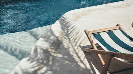 A peaceful poolside deck in the shade of a palm tree illustrates how beachfront homes create inviting outdoor retreats perfect for summer living.