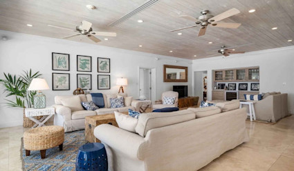 Living area with two cream colored couches facing each other with multiple ceiling fans and a media area with a flat screen tv.