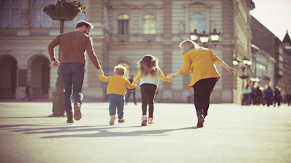 A family of four walks hand in hand through a Parisian city square, surrounded by historic architecture. This image evokes the essence of generational bonding and togetherness, aligning powerfully with the concept of anchoring family traditions in beautiful destinations.