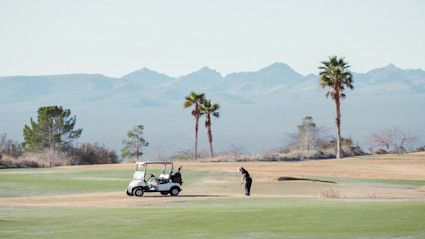 A golfer tees off against a mountain and palm backdrop, reflecting the leisure and beauty of living near championship courses.