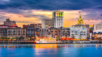 A ferry sits on the water with Savannah, Georgia’s skyline in the background, embodying why it’s one of the best places for a second home.