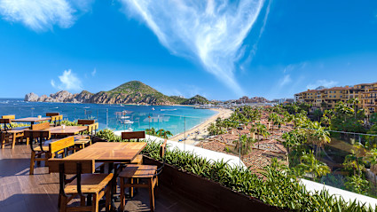 A stock photo shows an outdoor dining area overlooking the ocean with a mountain in the distance.