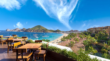 A stock image shows an outdoor patio overlooking the beaches and mountains of Cabo.