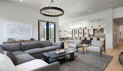 Living area with grey couch surrounding a small coffee table with kitchen with stainless steel appliances.