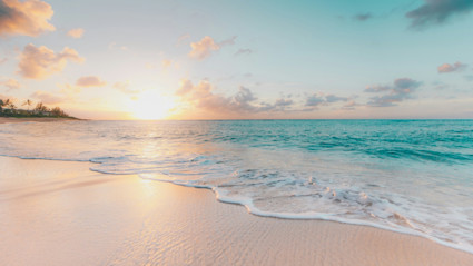 View of white sand beach with turquoise water with the sun setting.