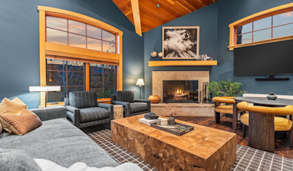 Living area with high ceiling and teal walls with mixed furniture arranged around a coffee table in front of a fireplace.