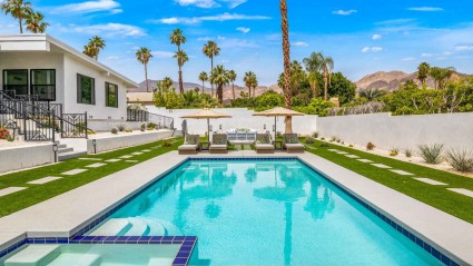 A second home pool on a a manicured lawn with lounge chairs and palm trees in the background