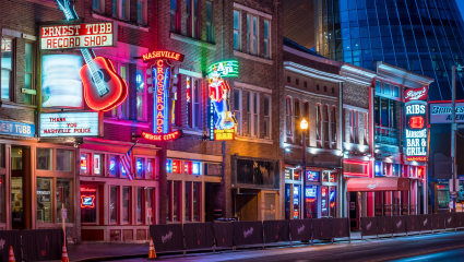 Neon signs hang over the sidewalk of downtown Nashville, Tennessee, embodying why it’s one of the best places for a second home.