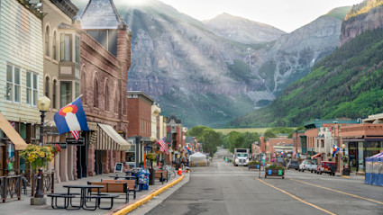 The shops of Telluride lining an empty street with green mountains in the background.