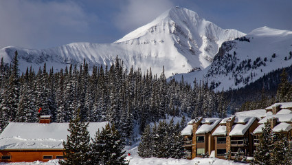 Snow covered buildings sit at the base of a white capped mountain in Big Sky, Montana, embodying why it’s one of the best places for a second home.