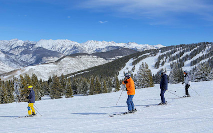 Skier carving down a sunny groomed run at Vail Mountain under a clear blue sky