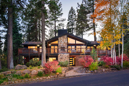 Modern mountain home with stone fireplace facade and wraparound deck, surrounded by pines and vibrant fall foliage in Lake Tahoe.