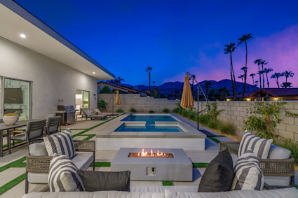 A luxury home's backyard in Palm Desert at dusk, featuring a lit pool, fire pit, and mountain views, creating a perfect atmosphere for private entertainment.